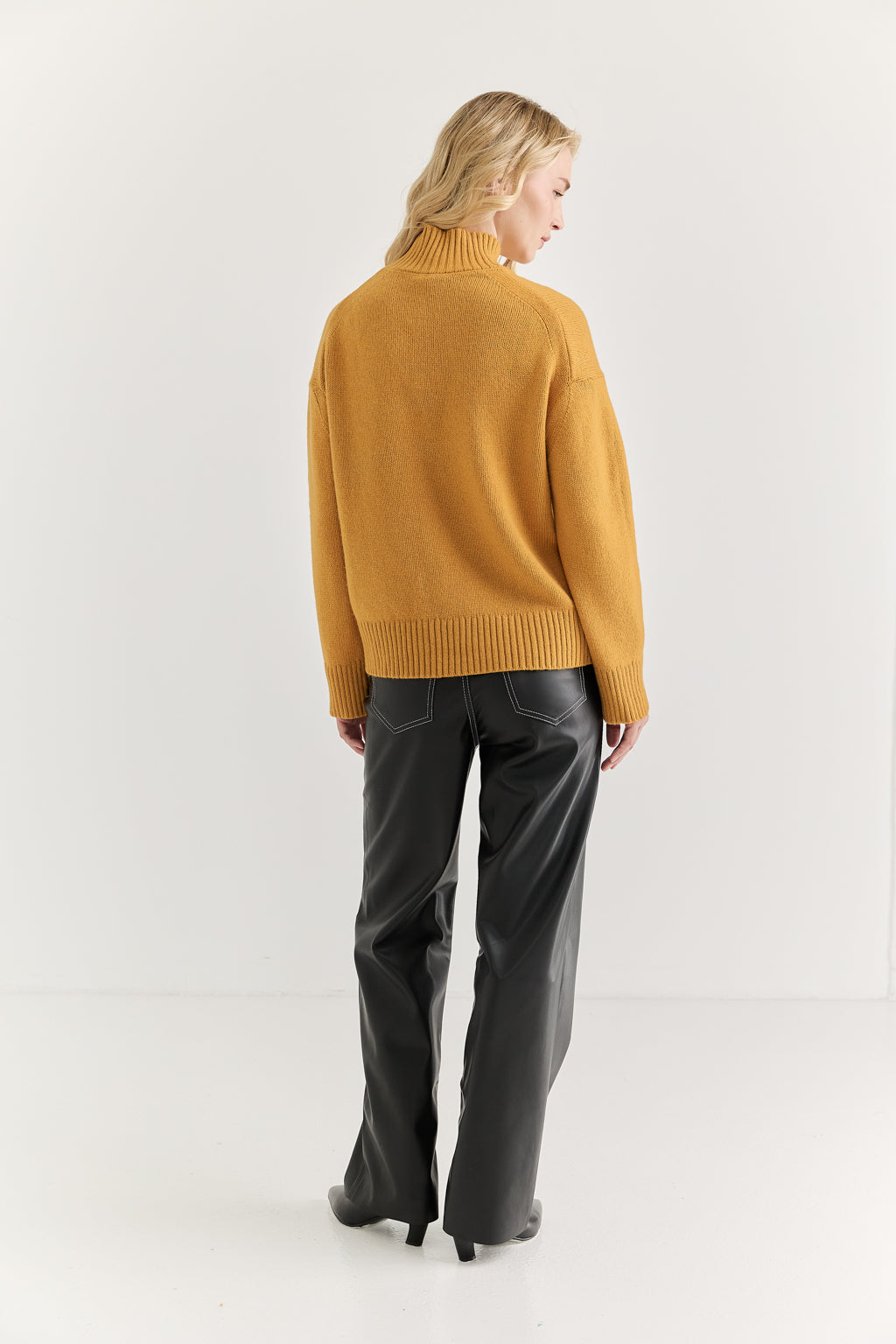 Person wearing a mustard yellow sweater and black pants on a white background