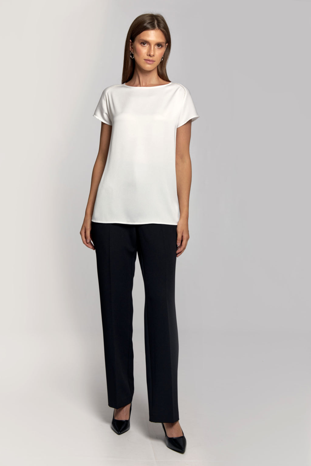 Woman wearing a white top and black pants on a light gray background