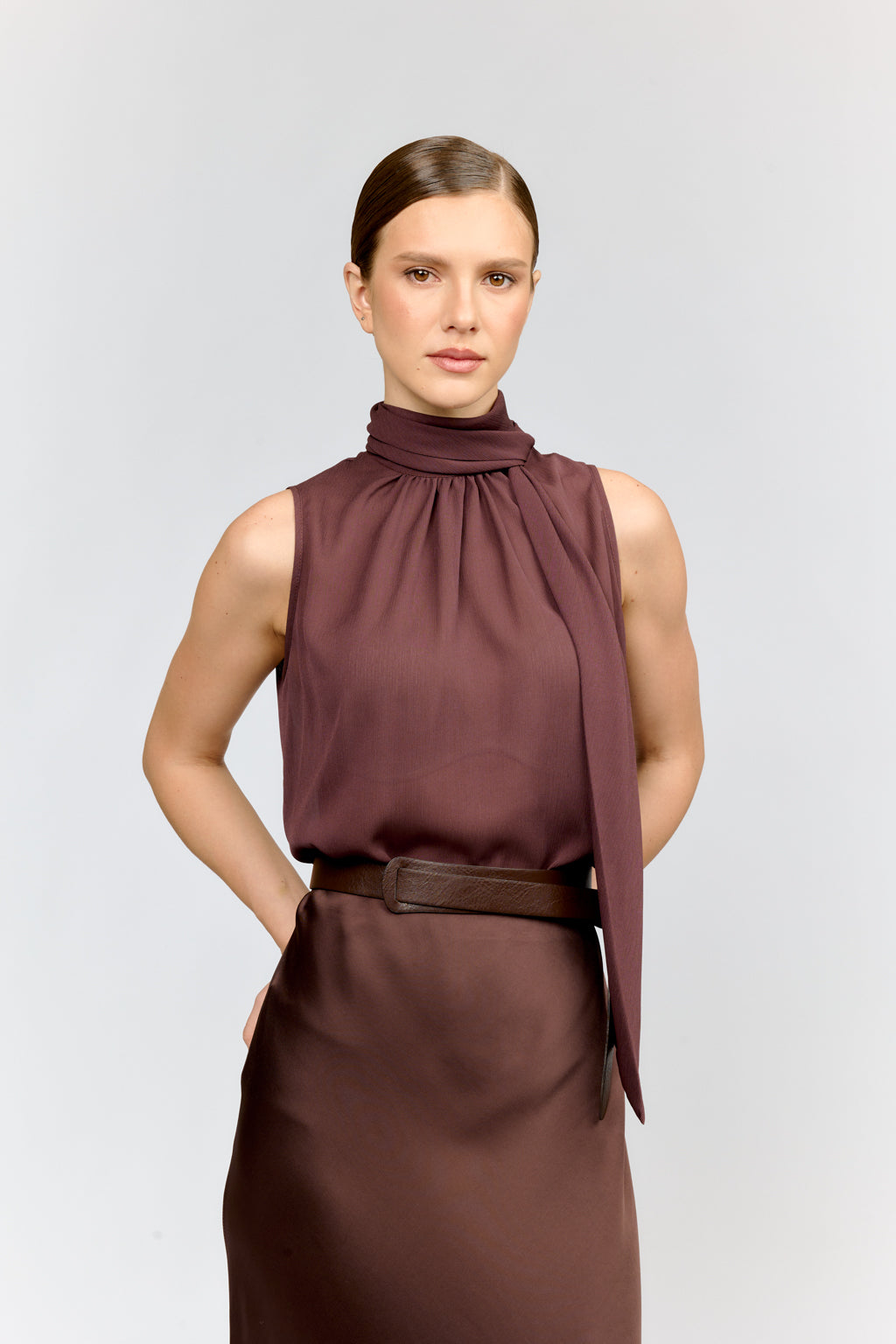Woman wearing a brown sleeveless top and skirt on a light gray background