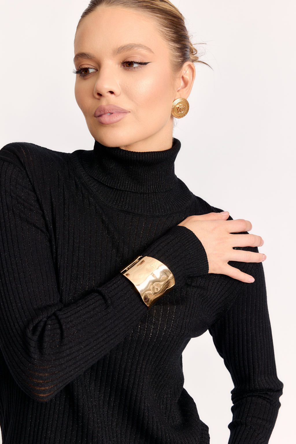 Woman wearing a black turtleneck sweater with gold accessories on a white background