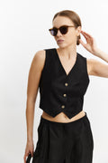 Woman wearing a black sleeveless top with buttons and black pants on a white background