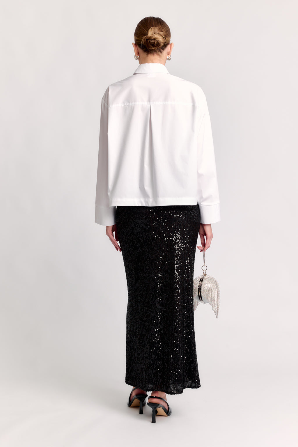 Person wearing a white shirt and black sequin skirt on a white background