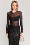 Woman wearing a black sheer top and sequin skirt with a neutral background