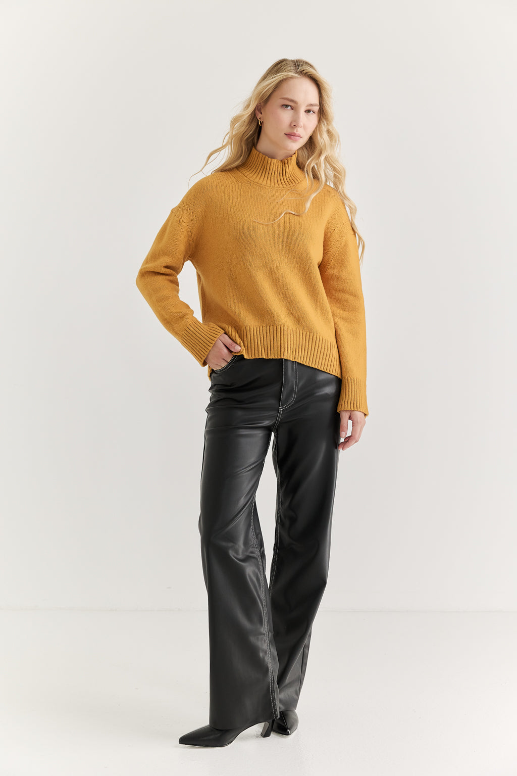 Woman wearing a mustard yellow sweater and black pants on a white background