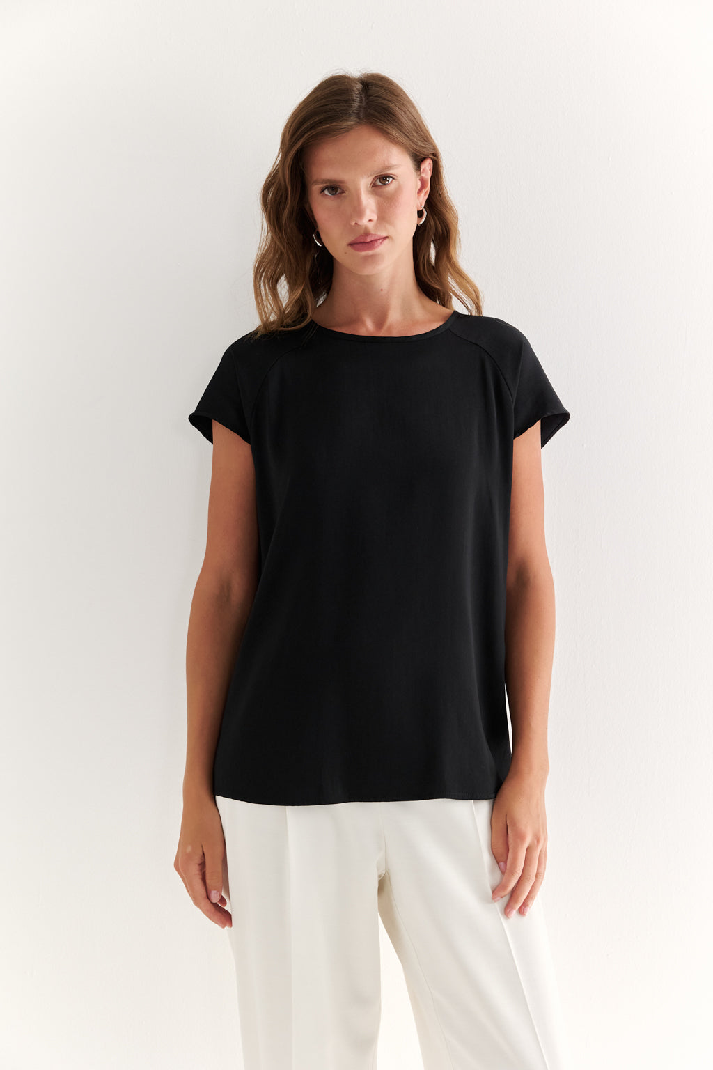 Woman wearing a black t-shirt and white pants on a white background