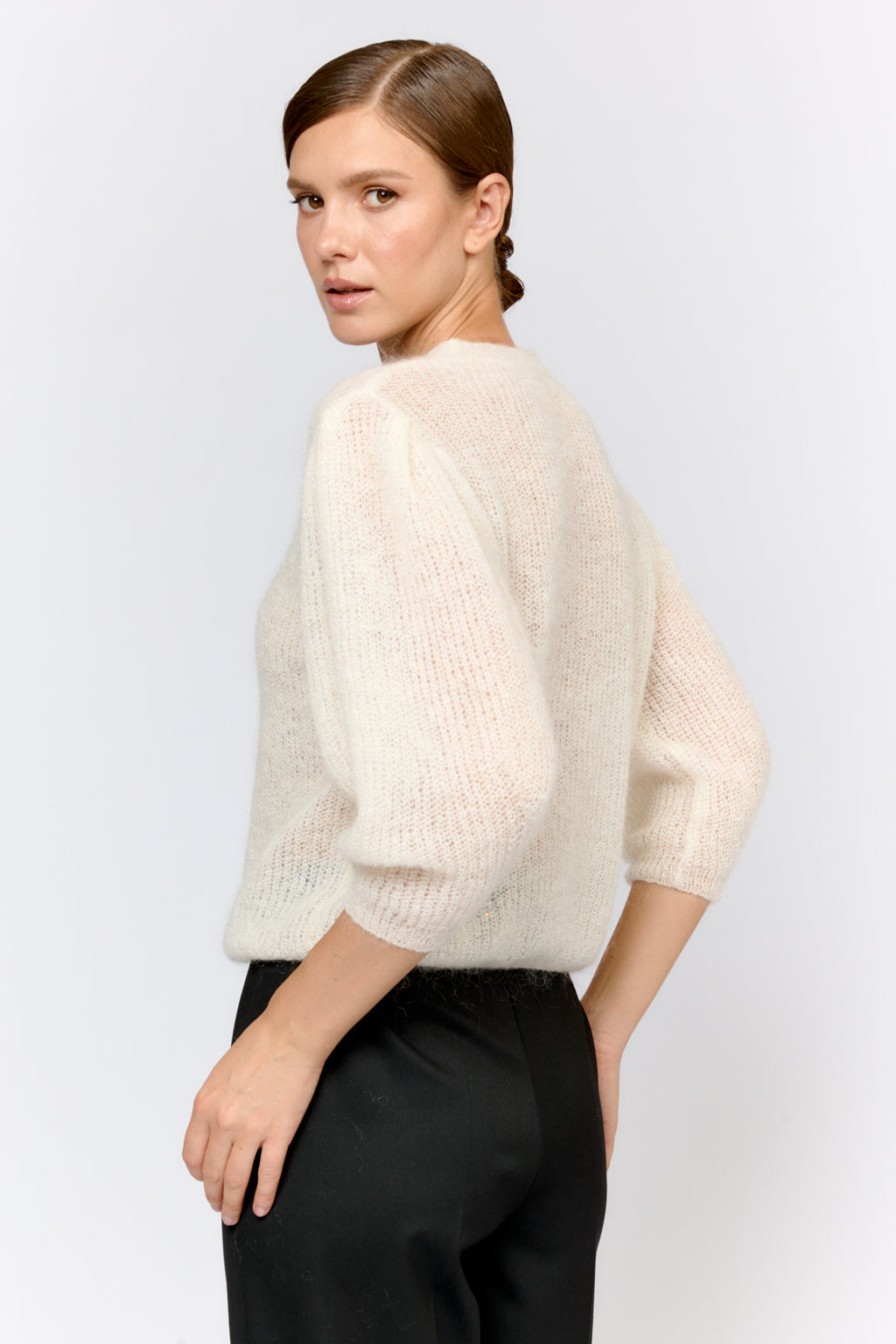 Woman wearing a light-colored sweater and dark pants on a white background