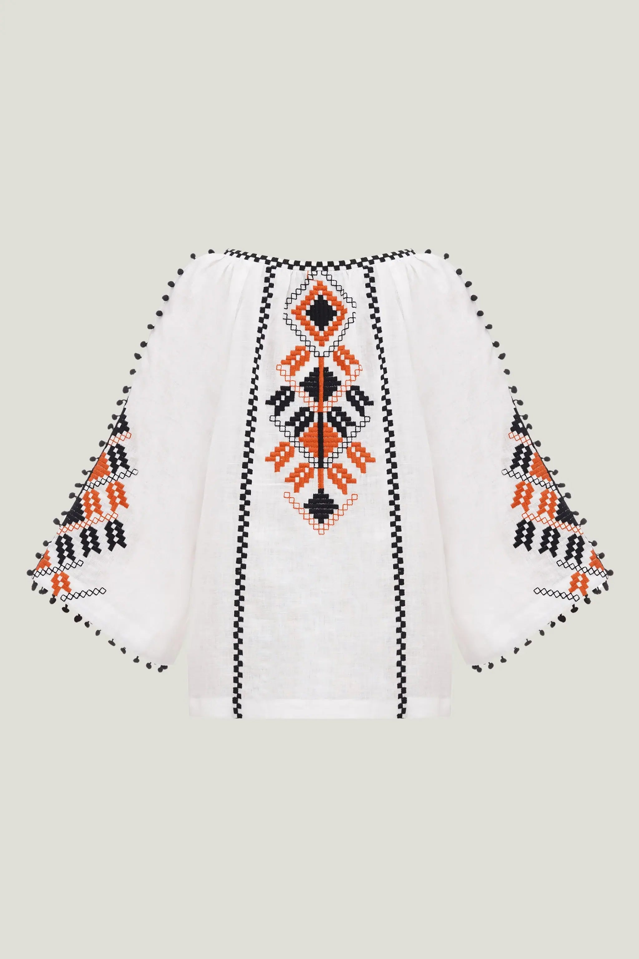 White embroidered blouse with geometric patterns in black and orange, featuring wide sleeves and a V-neckline, shown against a solid light gray background.