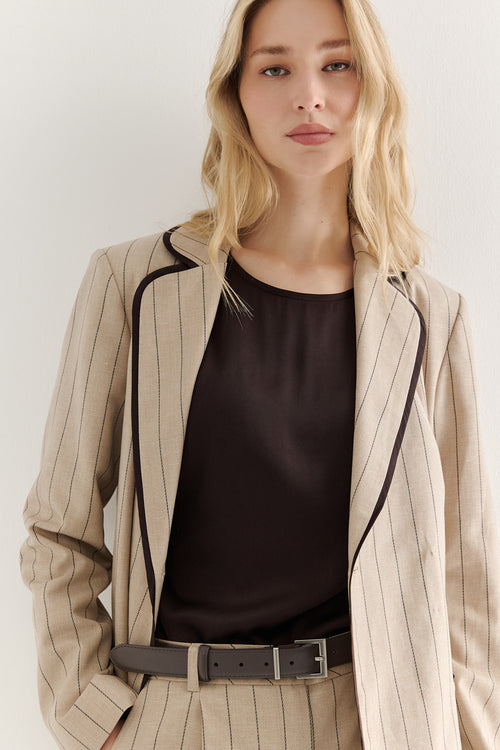 Woman wearing a beige pinstripe jacket over a black top on a white background