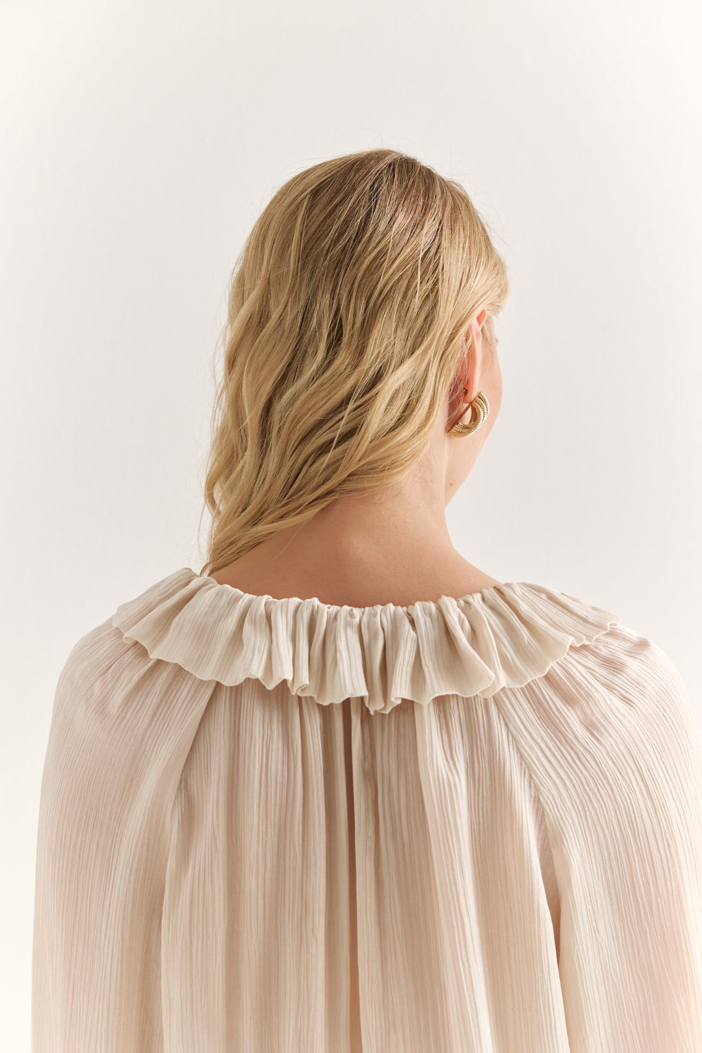 Woman wearing a beige blouse with ruffled collar against a white background