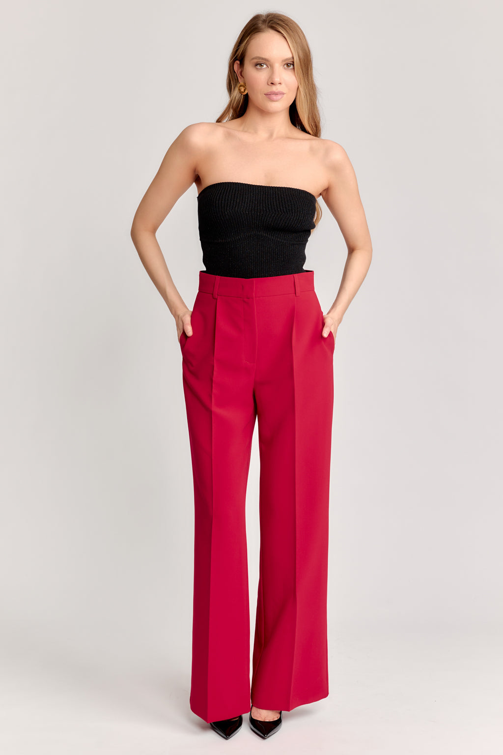 Woman wearing a black strapless top and red high-waisted pants on a light gray background