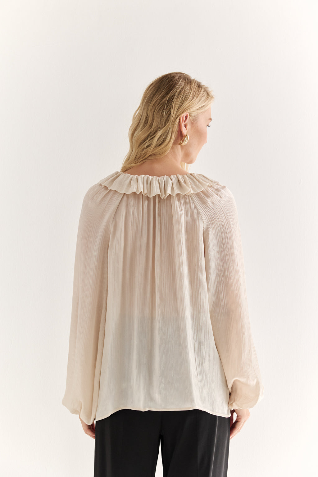 Woman wearing a beige blouse with a ruffled neckline on a white background