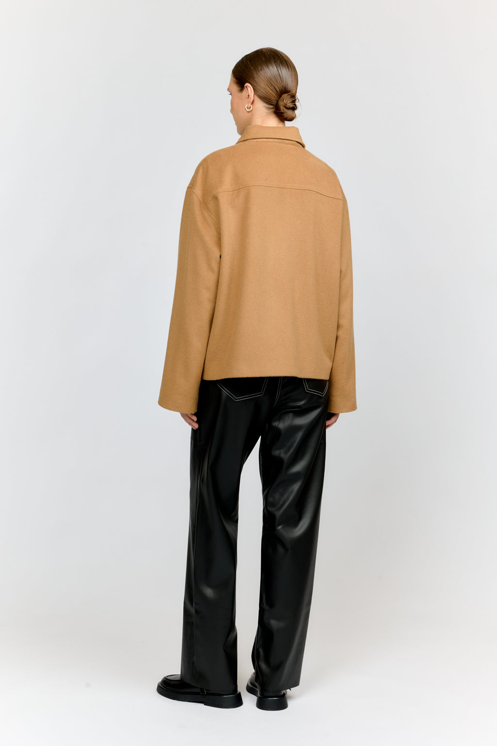 Person wearing a tan jacket and black pants on a white background