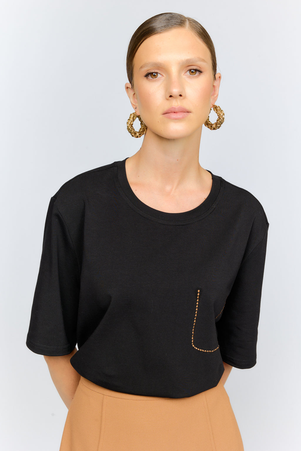 Woman wearing a black top with a pocket and tan pants against a white background