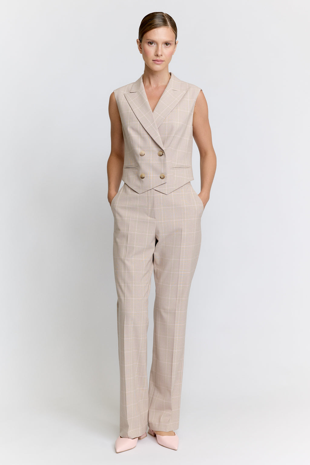 Woman wearing a beige suit vest and pants on a white background