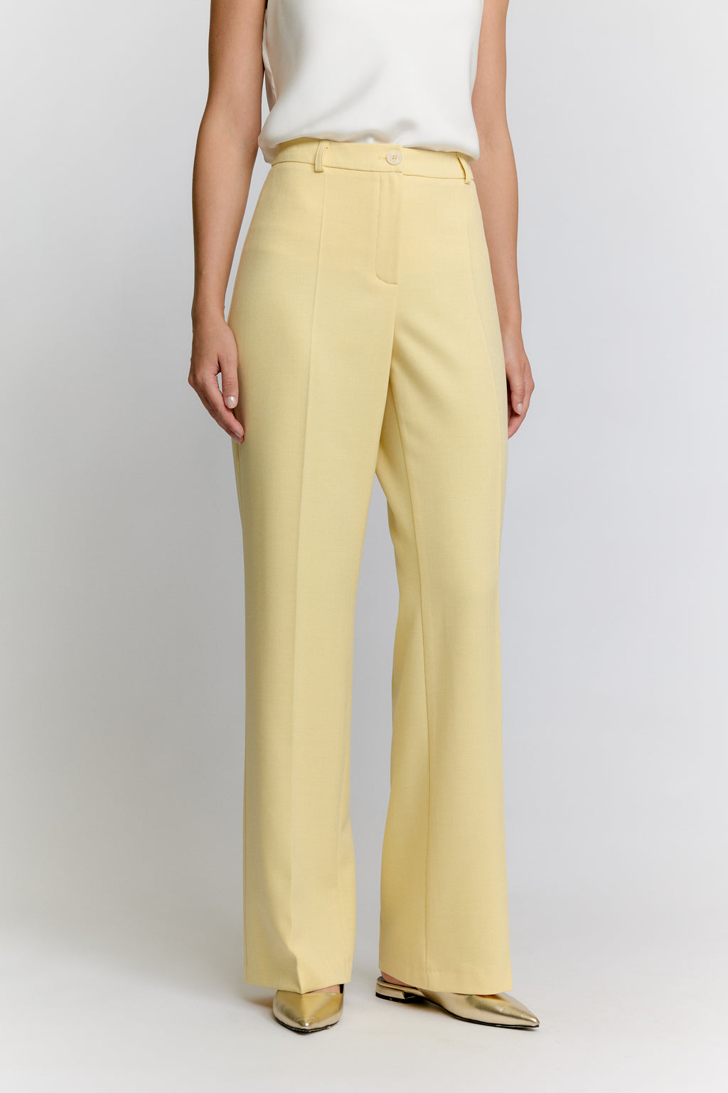 Person wearing light yellow pants and a white top on a plain background