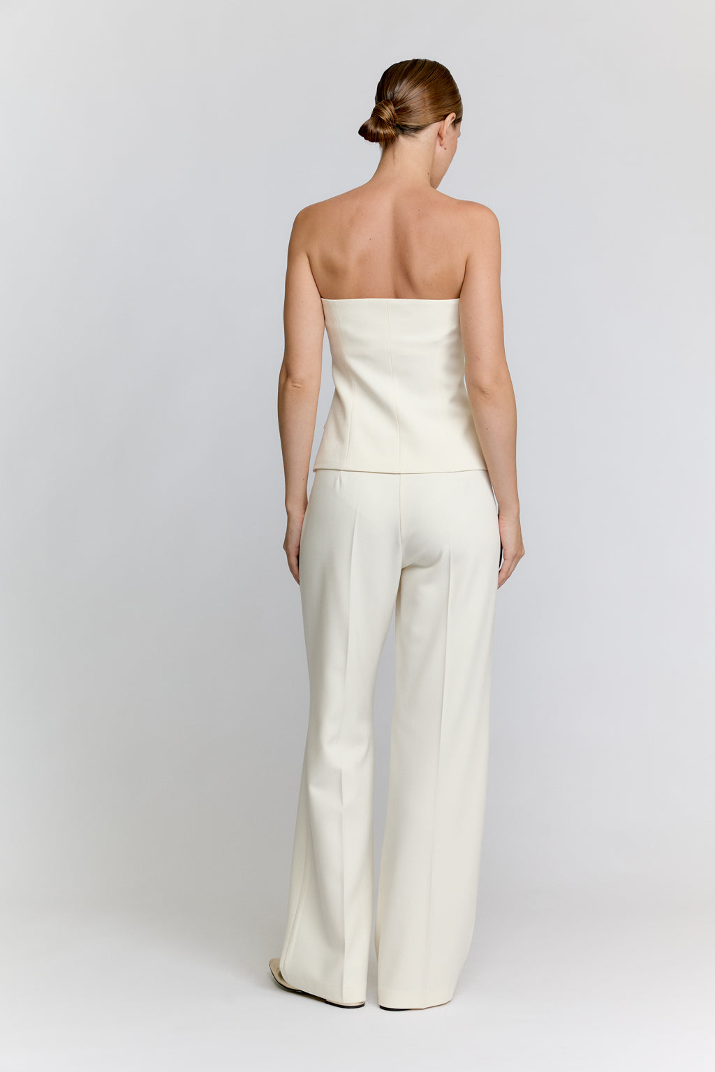 Woman wearing a white strapless jumpsuit on a plain background