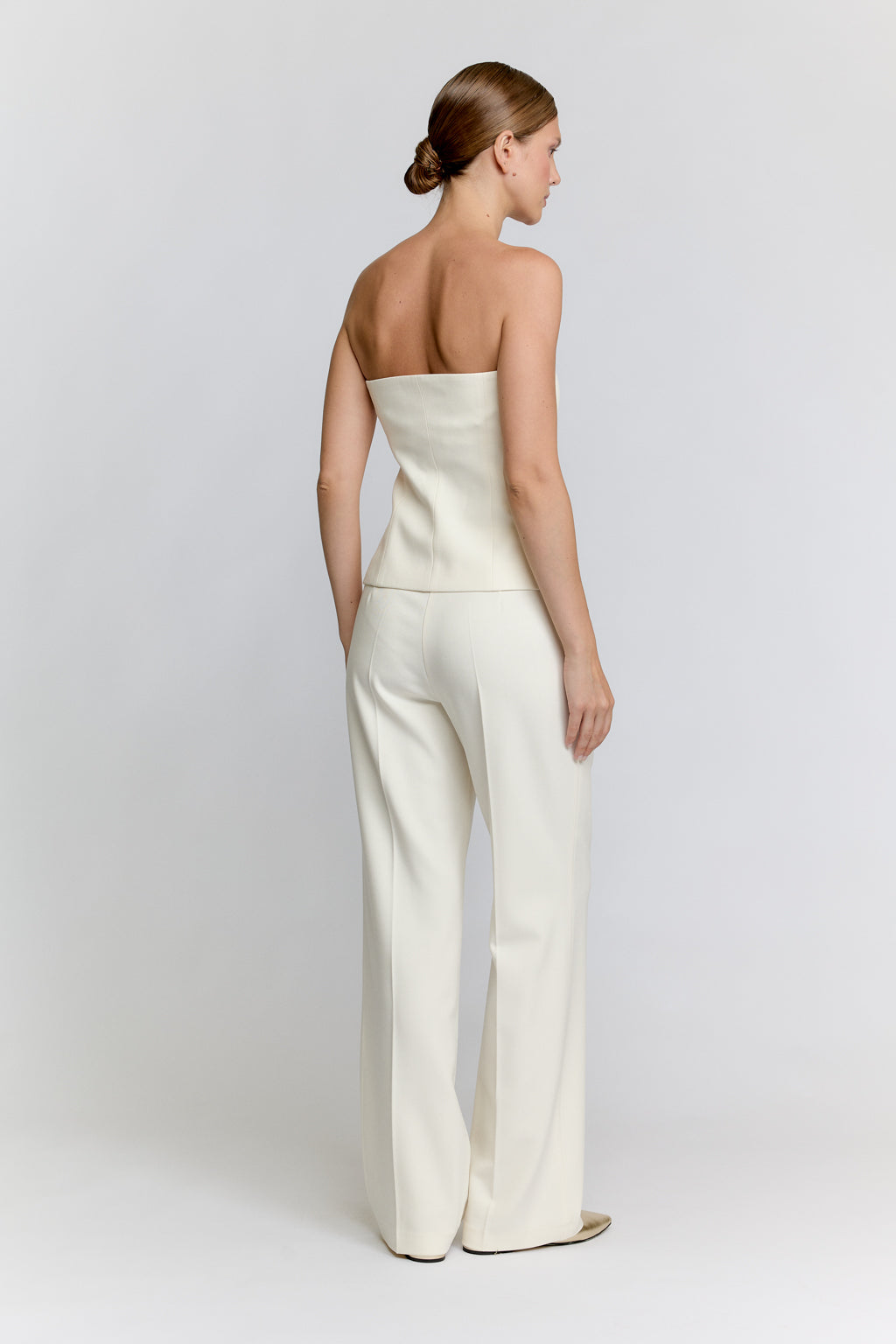 Woman wearing a strapless white jumpsuit on a plain background