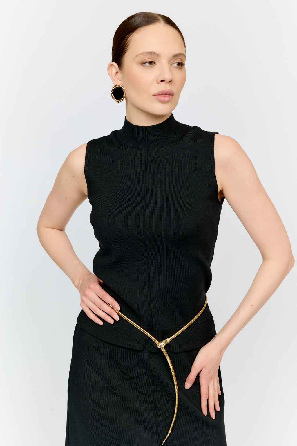 Woman wearing a black sleeveless top with a gold zipper on a light gray background