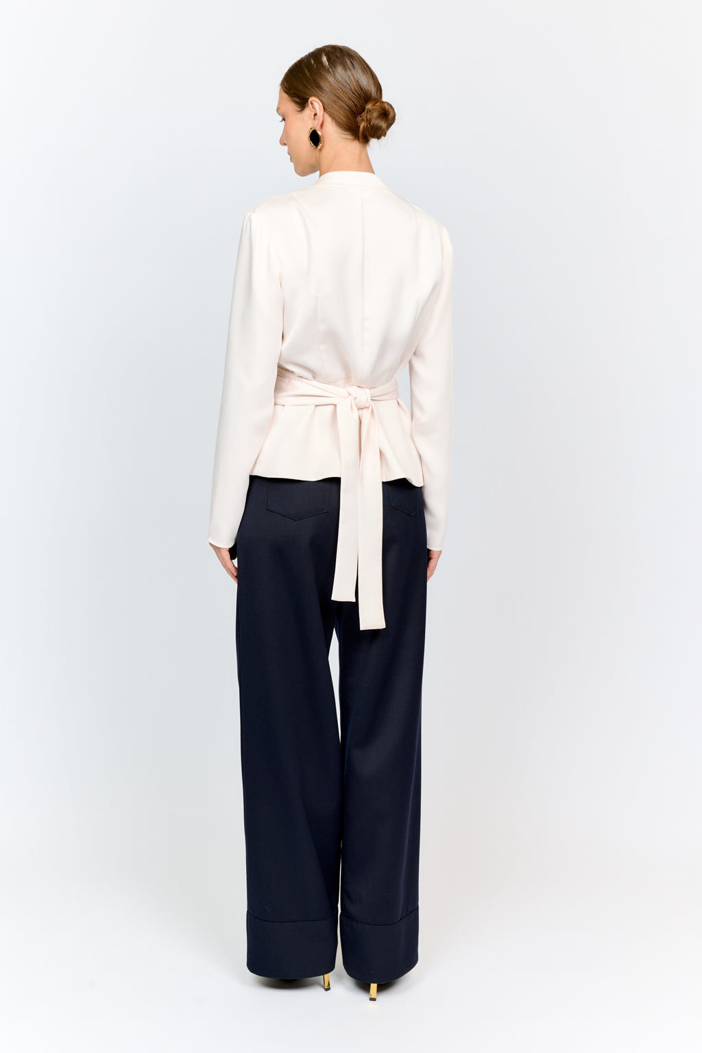 Woman wearing a white blouse with a belt and dark pants on a white background