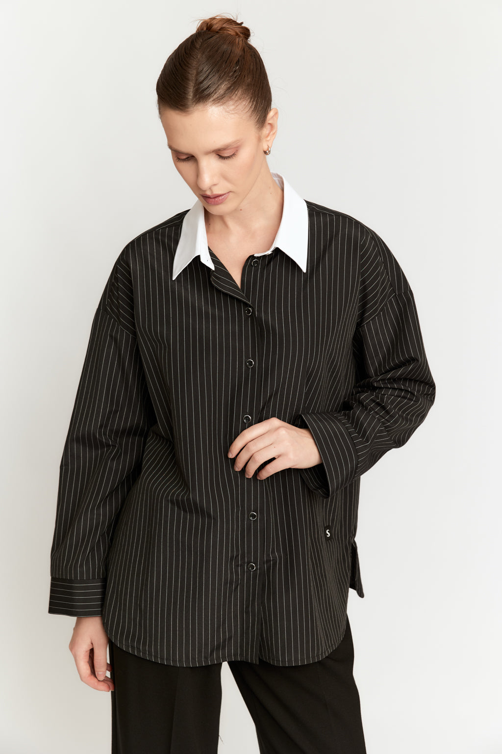Woman wearing a black pinstripe shirt with a white collar on a white background