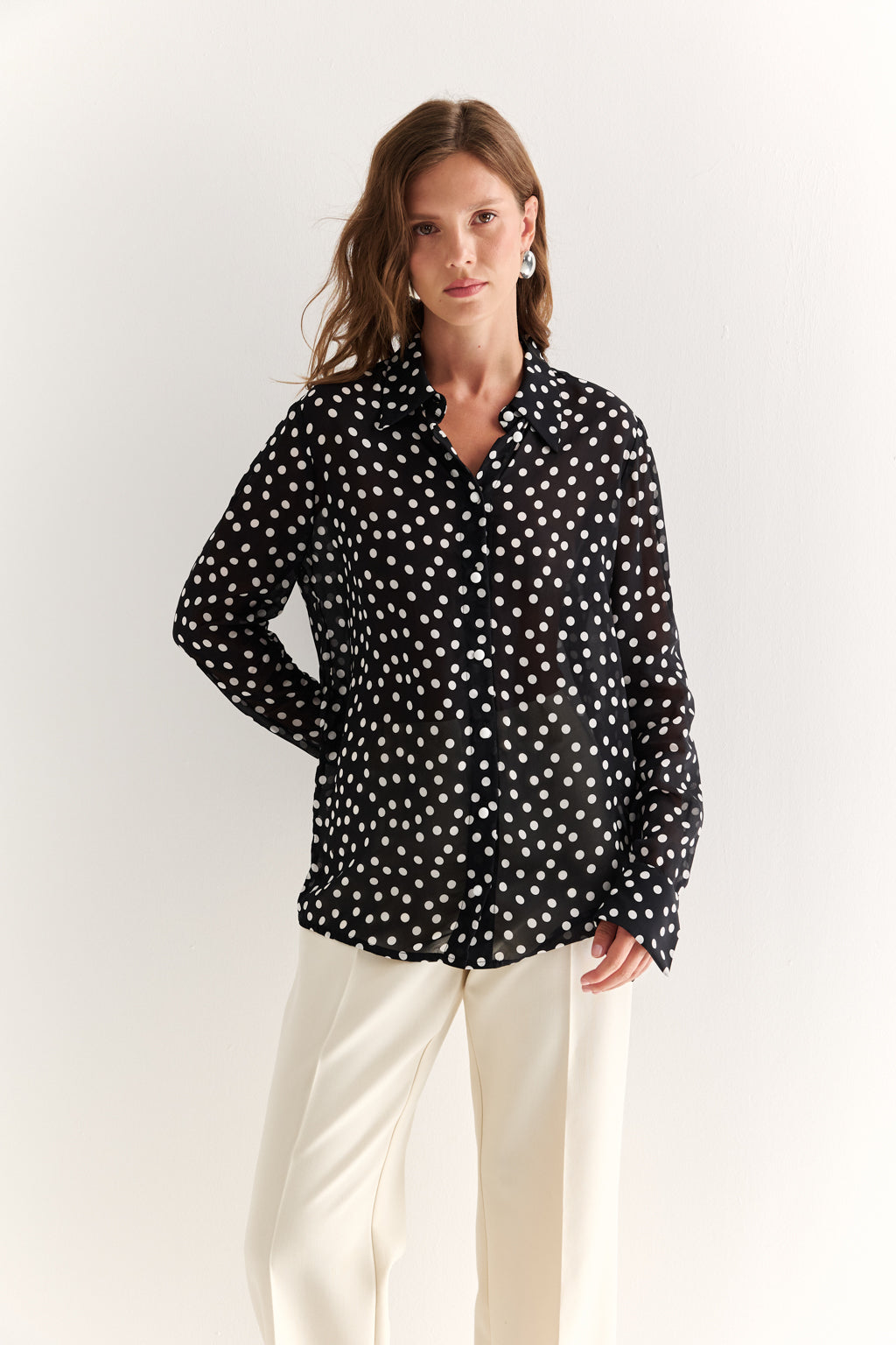 Woman wearing a black polka dot shirt and white pants on a plain background
