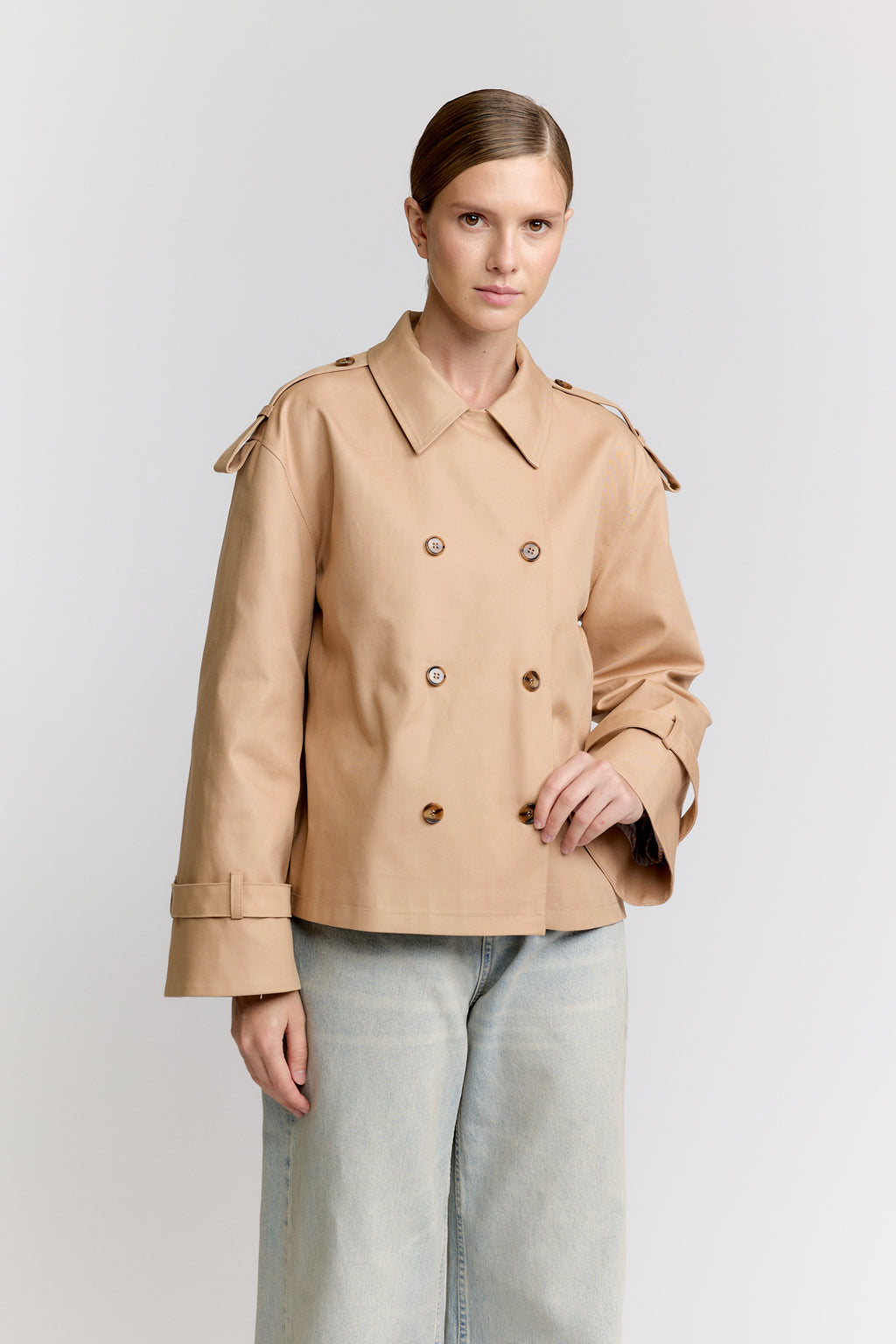 Woman wearing a beige trench coat on a light gray background