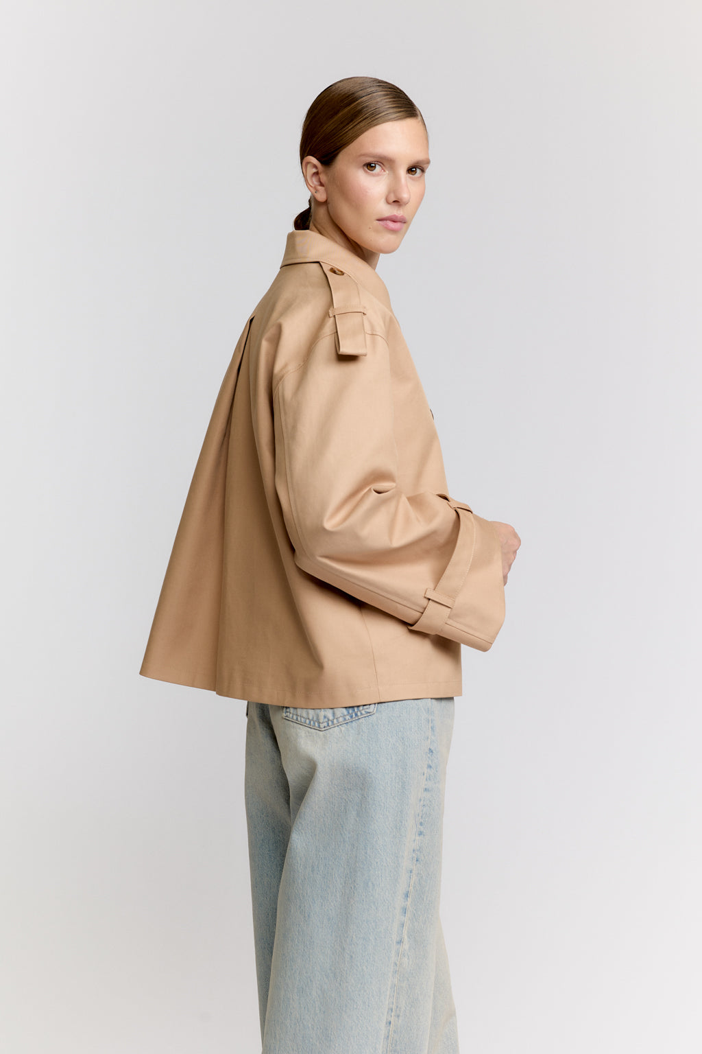 Woman wearing a beige coat and light blue jeans on a white background