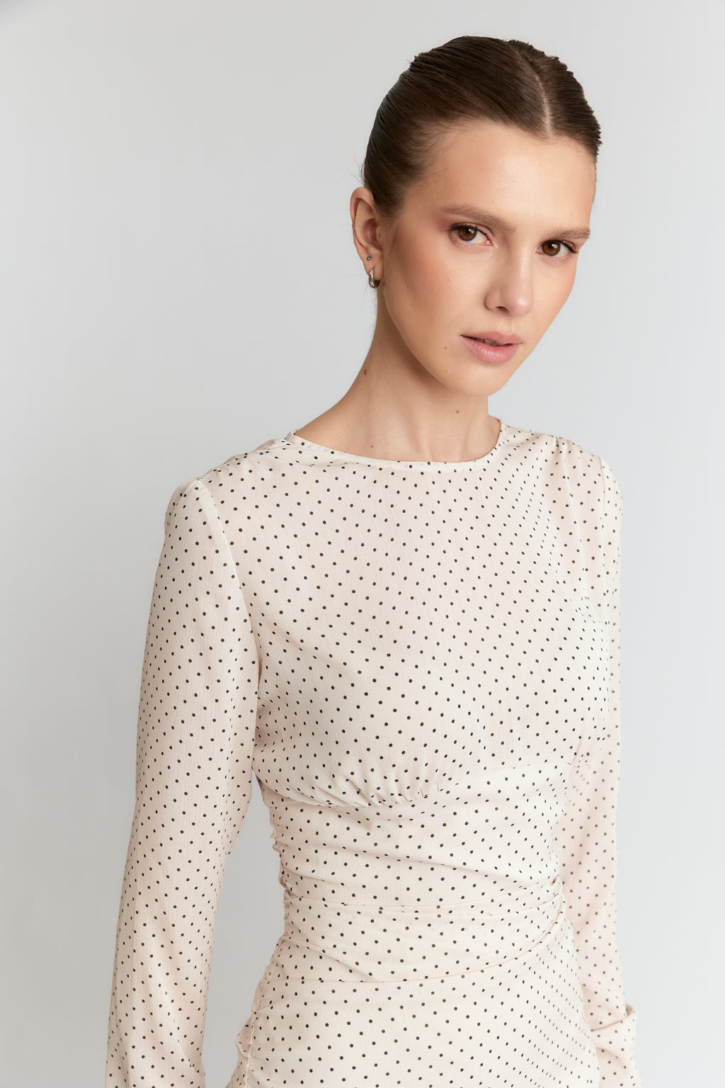 Woman wearing a white dress with black polka dots against a light gray background