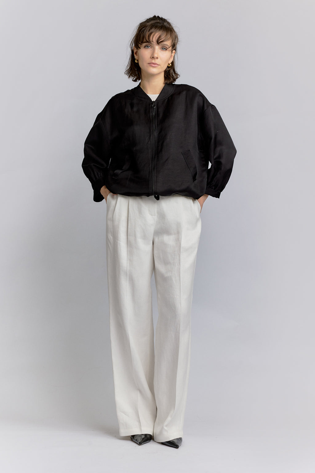 Person wearing a black jacket and white pants on a gray background