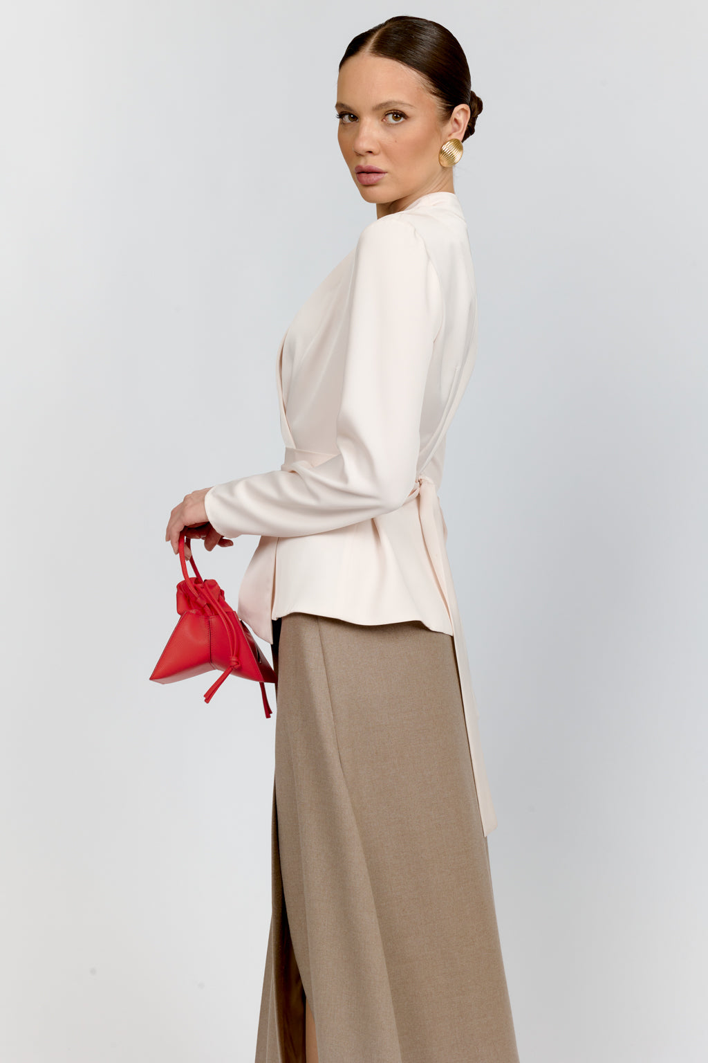 Woman holding a red handbag wearing a white top and beige skirt on a light gray background