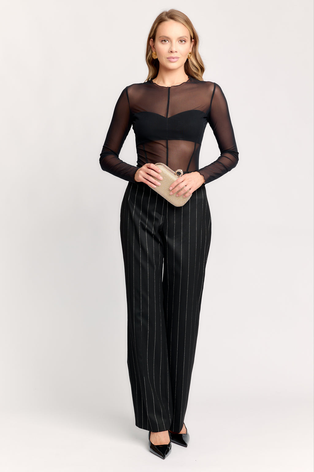 Woman wearing a black sheer top and pinstripe pants on a white background