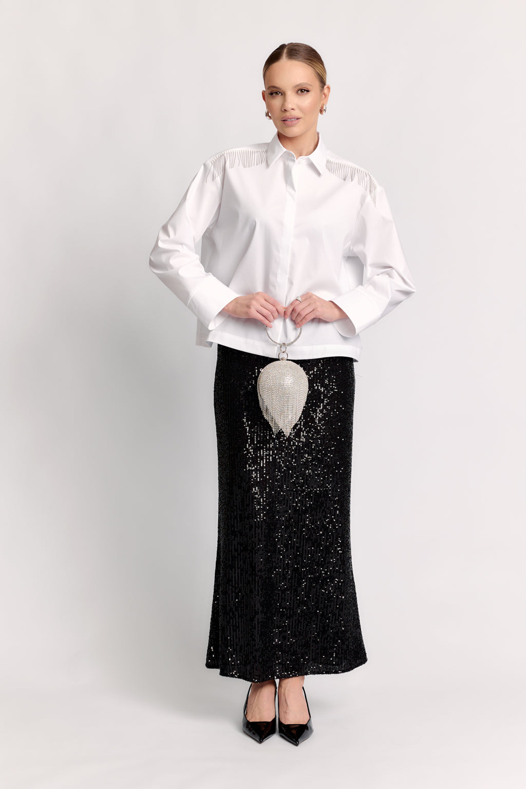 Woman wearing a white blouse and black skirt with a clutch on a light gray background