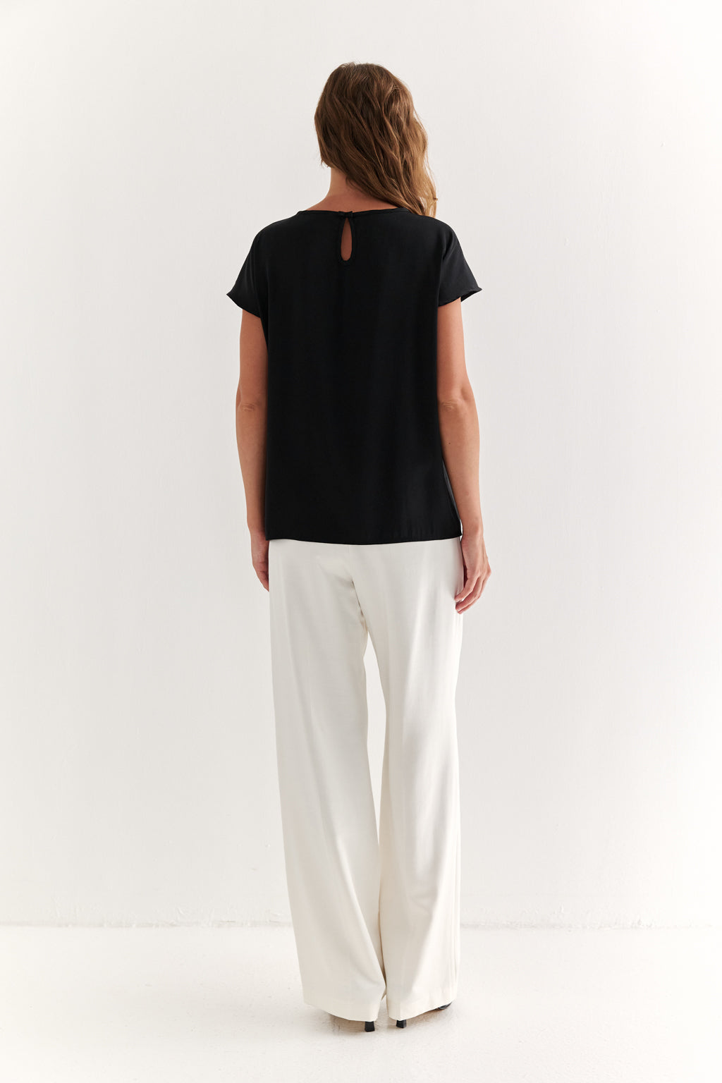 Woman wearing a black top and white pants on a white background