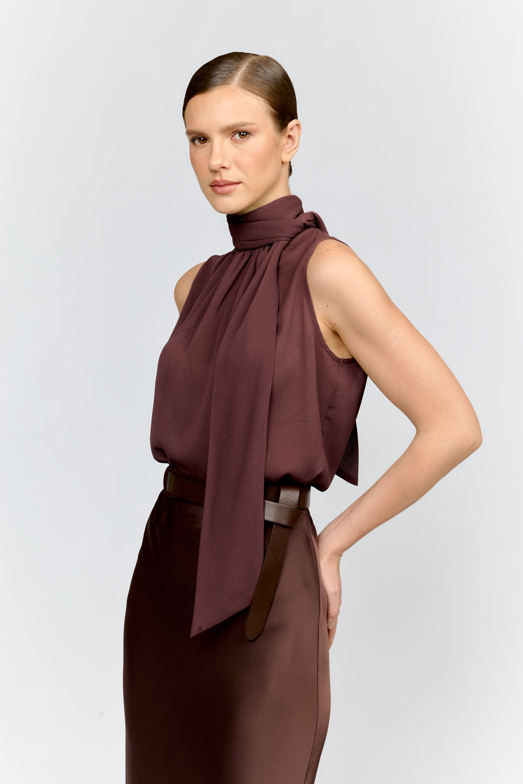 Woman wearing a brown sleeveless top with a scarf and skirt on a light gray background