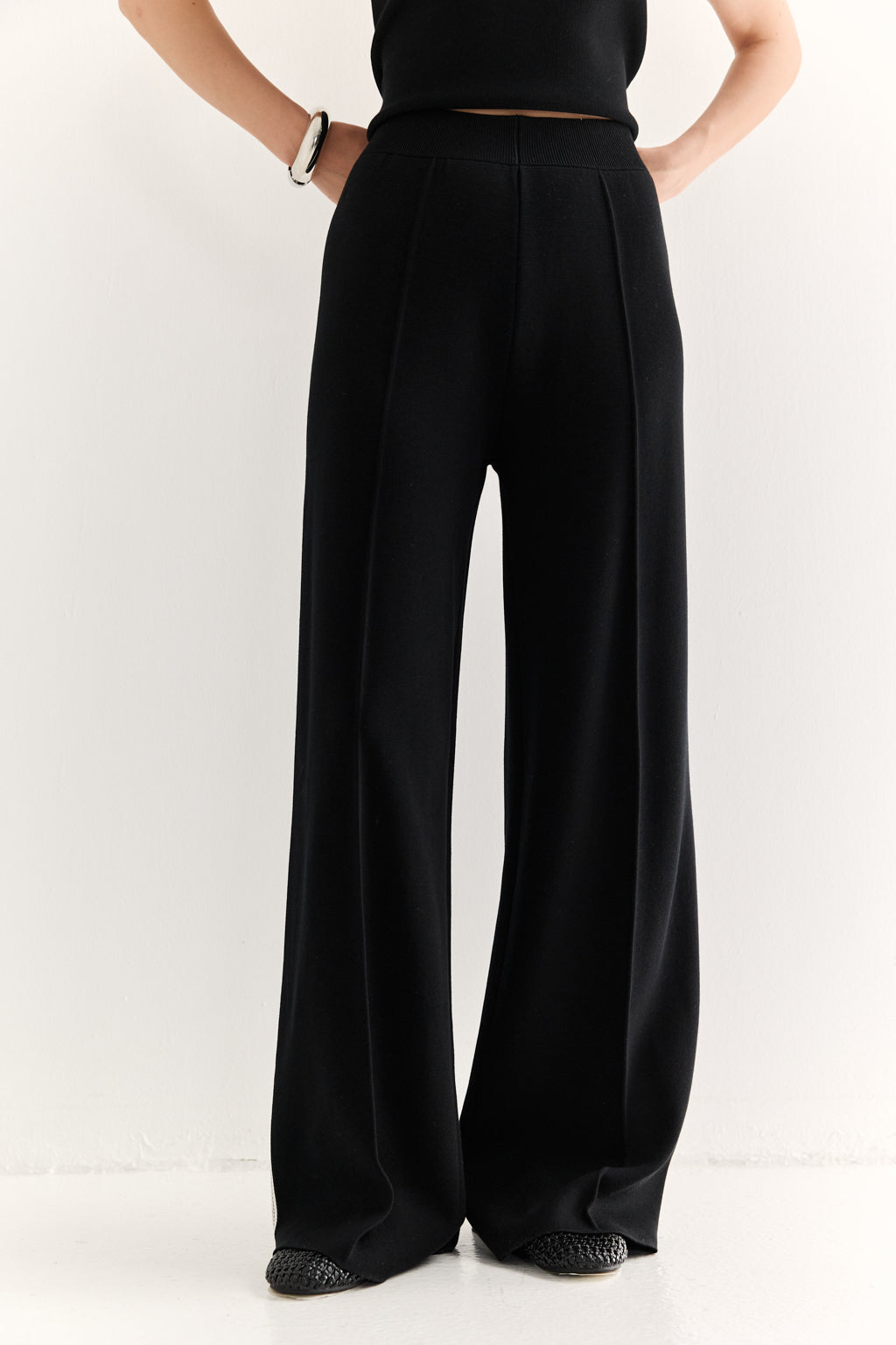 Person wearing black wide-leg pants on a white background