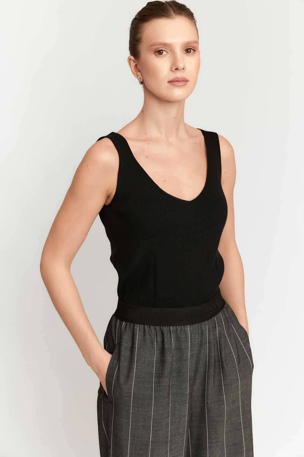 Woman wearing a black sleeveless top and gray plaid pants on a white background