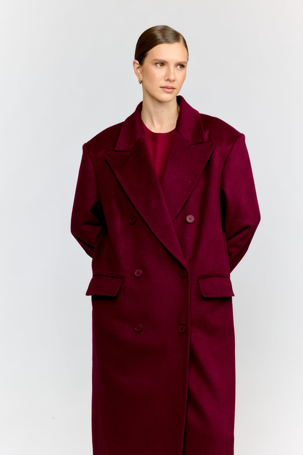 Woman wearing a burgundy coat and dress against a white background