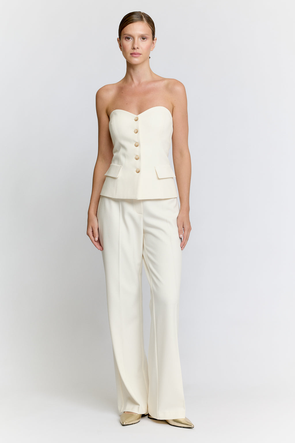 Woman wearing a white strapless top and wide-leg pants on a plain background